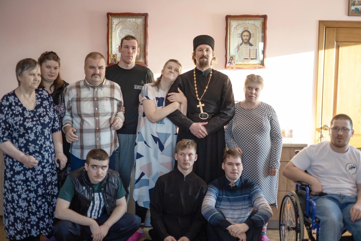 Священник в окружении людей - жителей Дома