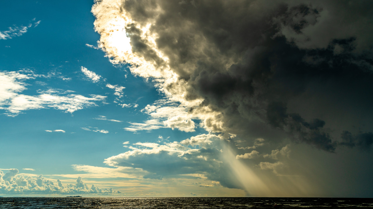 Солнце просвечивает сквозь грозовую тучу, над морем