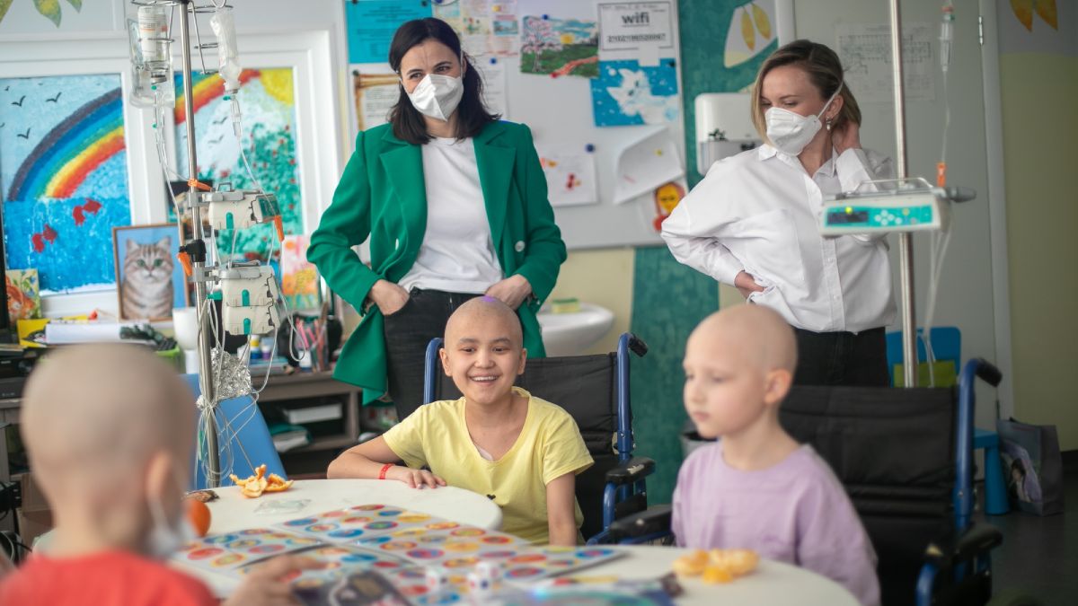 Маленькие онкопациенты сидят за столом. Сзади стоят две женщины.