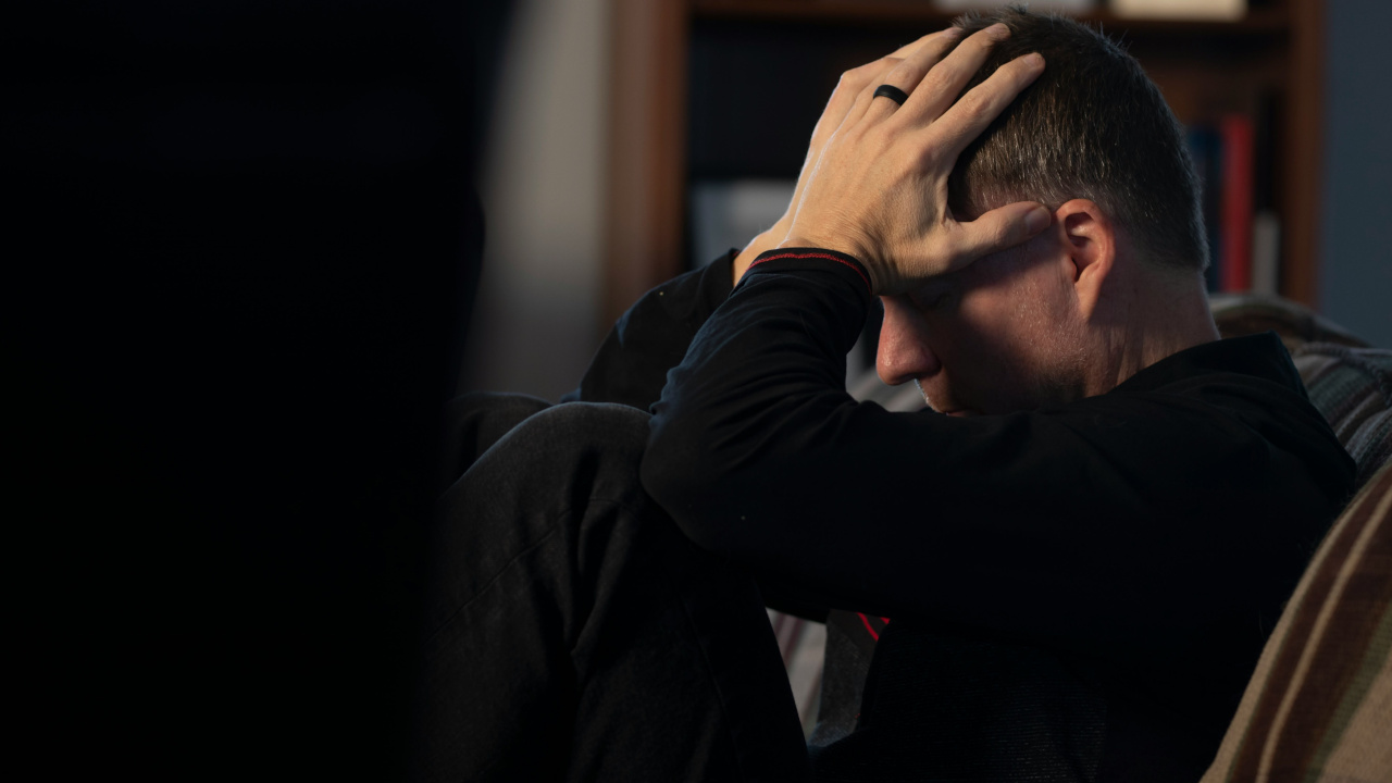 Мужчина держится за голову сидя на диване